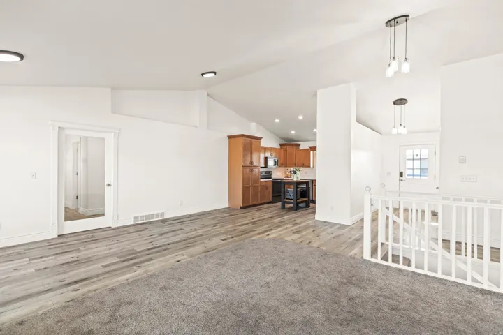 Vaulted ceiling, recessed lighting, wood-finish flooring, white railing, and kitchen with wood cabinetry