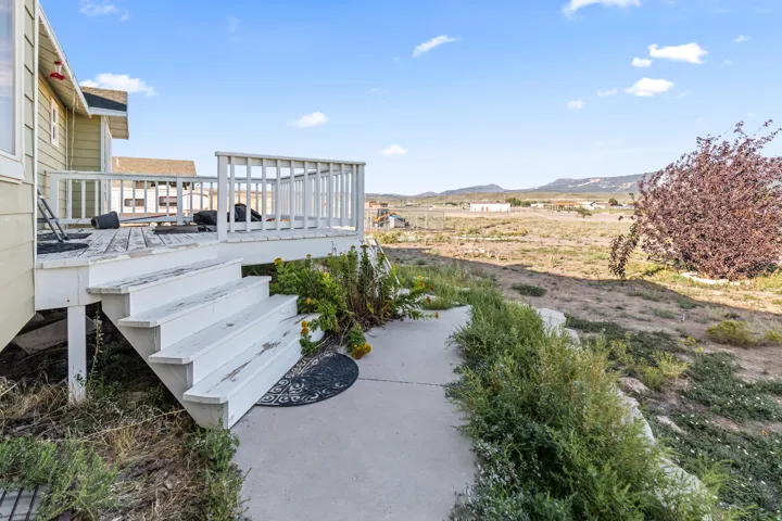 Exterior deck with white railing, three-step staircase, and a concrete pathway
