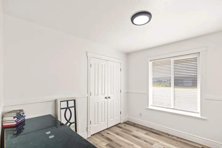 Room featuring wood-finish flooring, a window with blinds, white trim, a flush-mount ceiling light, and a double-door closet