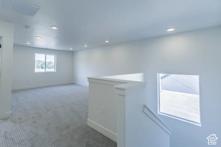 Upper-level landing with recessed lighting, light-colored carpeting, white walls, and bright windows