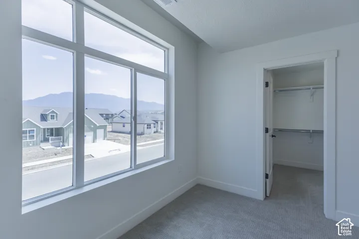 Bright corner bedroom with expansive multi-pane windows framing mountain and neighborhood vistas, neutral carpet flooring, and an adjoining walk-in closet with shelving systems