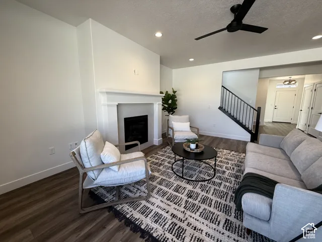 Living area featuring a fireplace with a white mantel, dark wood-finish flooring, recessed lighting, and a black ceiling fan