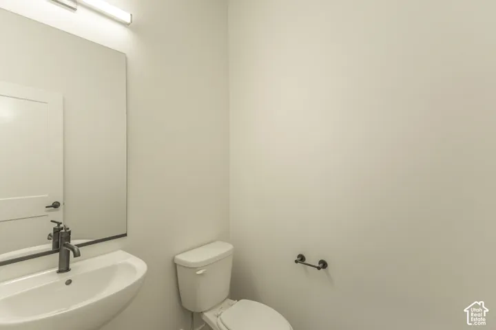 Clean, functional half bath featuring a curved ceramic sink, porcelain toilet, and chrome wall-mounted fixtures