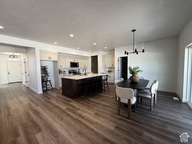 Wood-finish flooring throughout, kitchen featuring white cabinetry, dark wood-finish island with seating, pendant lighting, and a dining area with a modern chandelier