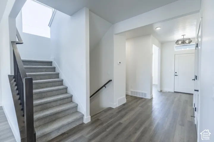 Inviting entryway with wood-finish flooring, a carpeted staircase with a dark wood handrail, and a decorative overhead light fixture
