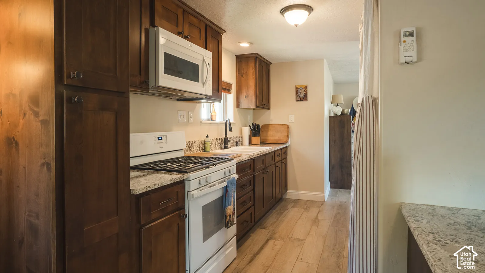 Kitchen featuring wood-finish cabinetry, light-toned countertops, tile flooring, and white appliances including a gas range and microwave