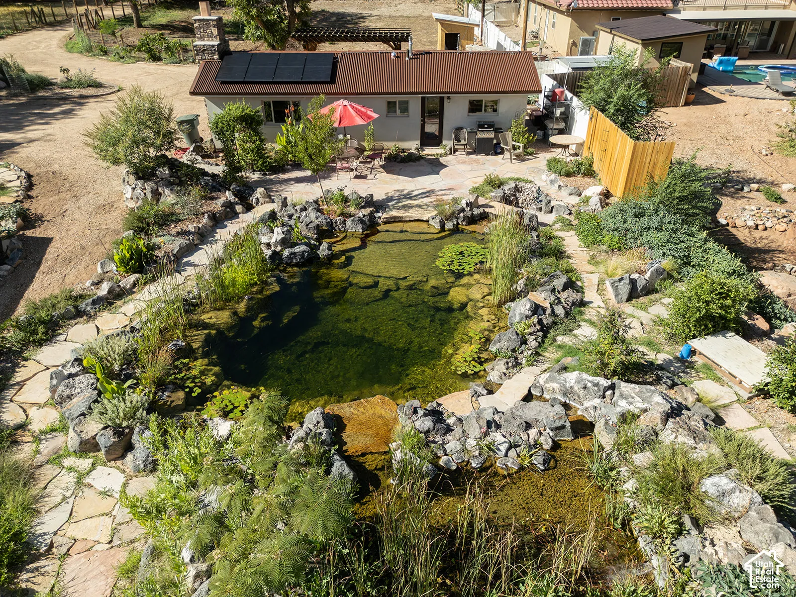 Property featuring a large pond with natural rock landscaping, flagstone pathways, a patio area, and a structure with solar panels