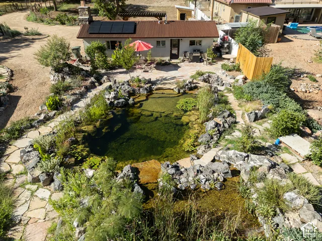 Property featuring a large pond with natural rock landscaping, flagstone pathways, a patio area, and a structure with solar panels