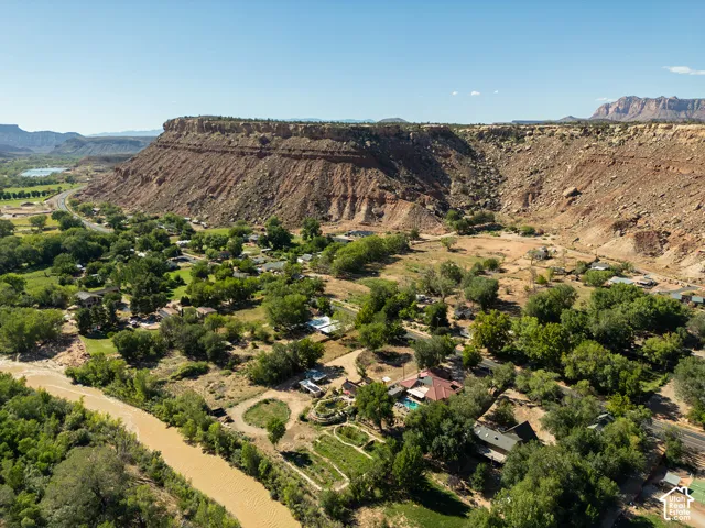 Expansive desert landscape featuring a prominent mesa, a winding river, and numerous mature trees
