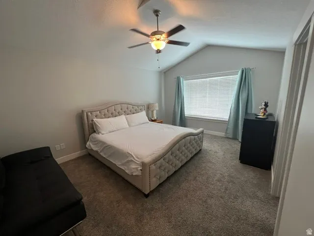 Vaulted ceilings with a ceiling fan light fixture, carpeted flooring, and a large window with blinds