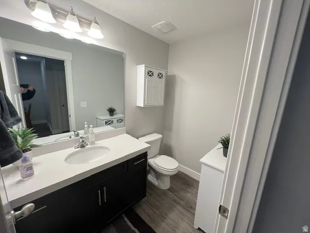 Bathroom featuring a dark wood-finish vanity with a white countertop and integrated sink, a large wall-mounted mirror, and wood-finish flooring