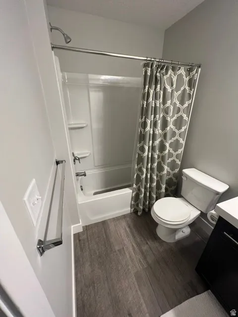 Full bathroom featuring a white tub and shower combination with chrome fixtures, a white toilet, and wood-finish flooring