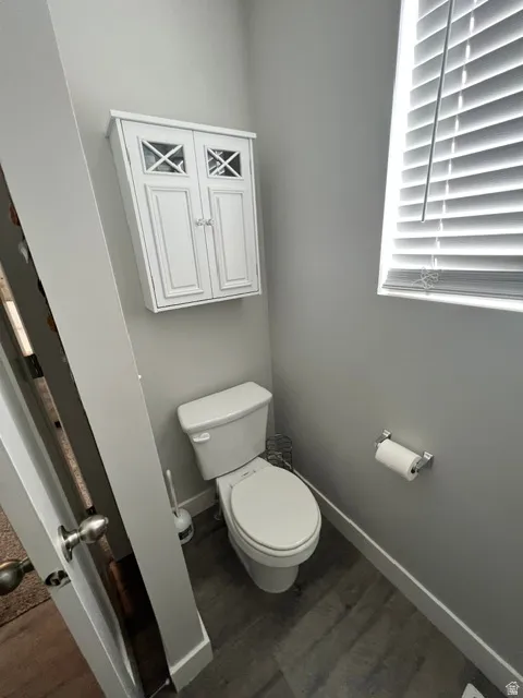 Powder room featuring wood-finish flooring, a white toilet, and a window with blinds