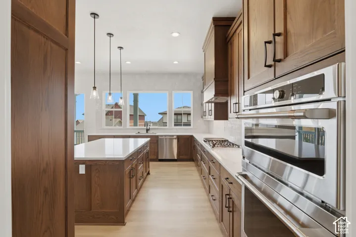 Kitchen featuring wood-finish cabinetry, stainless steel appliances, a center island with a white countertop, recessed lighting, and pendant lighting