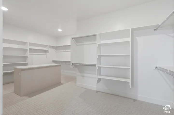 Spacious walk-in closet featuring white built-in shelving, hanging rods, and a central island with a solid surface countertop