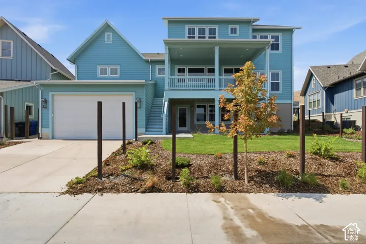 Turquoise siding exterior with multiple windows, an attached garage, a second-story balcony, and a ground-level patio, set on a landscaped lot with a concrete driveway