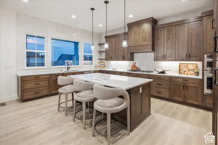 Kitchen featuring custom wood cabinetry, quartz countertops, central island, integrated stainless steel appliances, and large windows with natural lighting