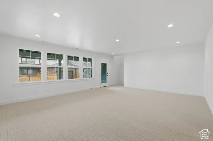 Recessed lighting, light-colored carpeting, multiple windows, white walls, and a glass-paneled door