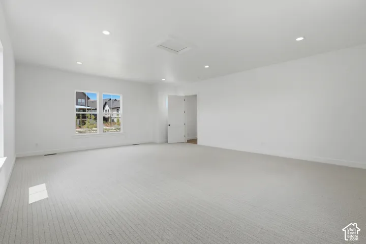 Spacious room featuring light-colored patterned carpeting, recessed ceiling lighting, and multiple windows