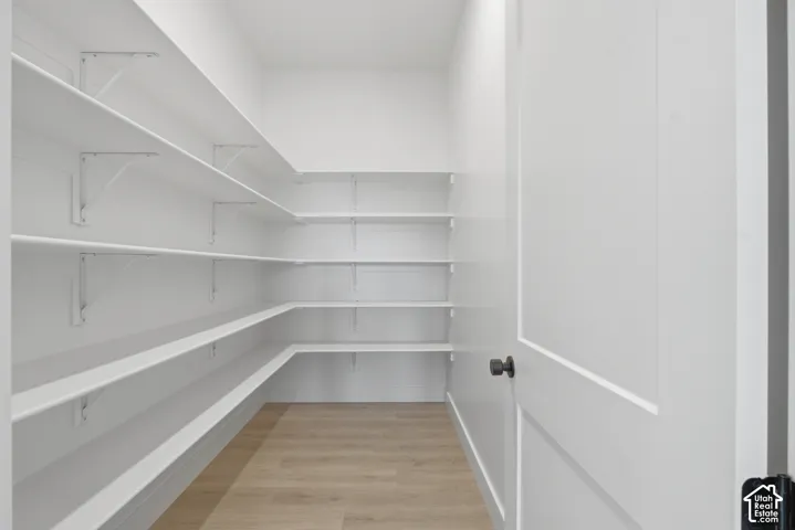 Walk-in pantry with extensive white shelving, light wood-finish flooring, and a white panel door with matte black hardware