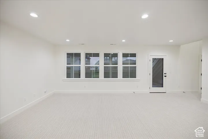 Neutral-toned carpeting, recessed ceiling lighting, four multi-pane windows, and a glass-panel exterior door
