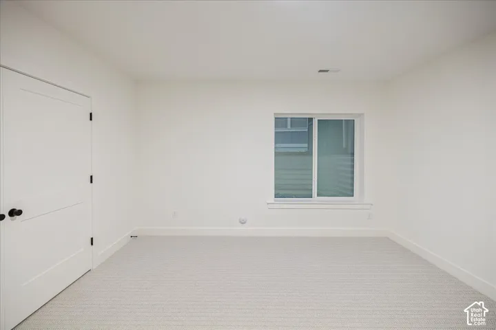 Neutral-toned wall-to-wall carpeting, crisp white walls, sliding window with a sill, and a single-panel interior door featuring matte black hardware