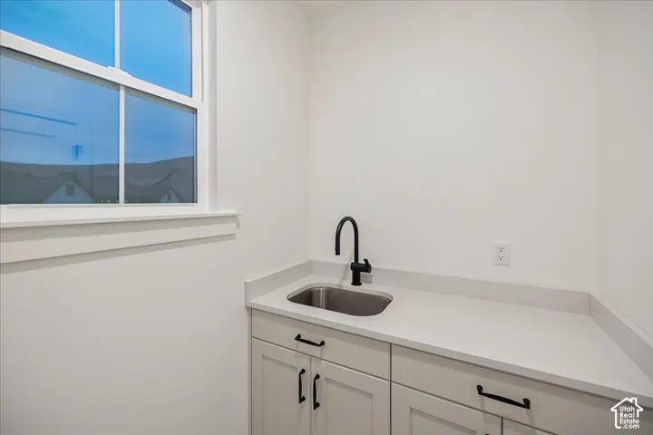 Utility room featuring white cabinetry, solid-surface countertop, stainless steel drop-in sink, and matte black hardware