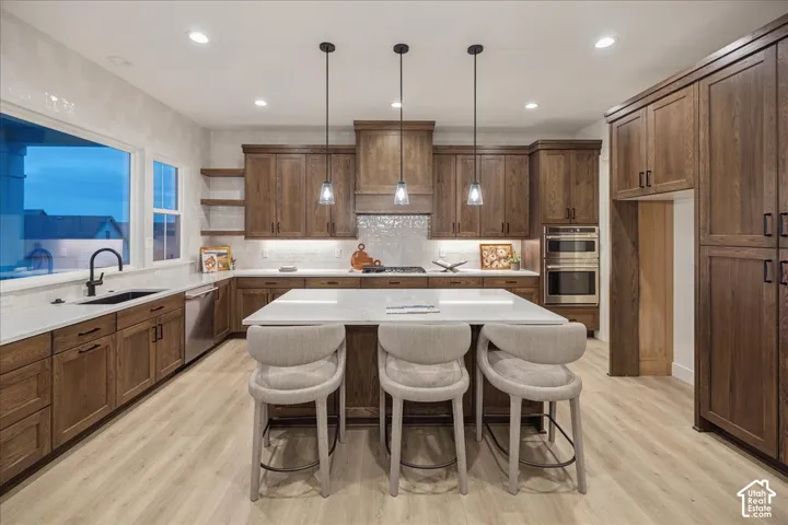 Kitchen featuring stained wood cabinetry, quartz countertops, a central island with a waterfall edge, tile backsplash, and stainless steel double wall ovens