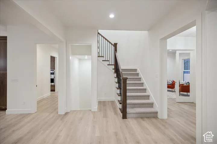 Interior staircase featuring a stained wood handrail, metal balusters, and carpeted treads, complemented by wood-finish flooring and recessed lighting