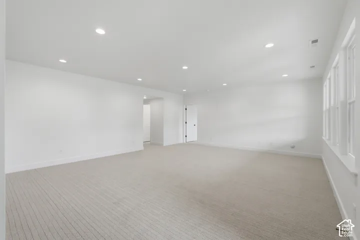 Recessed ceiling lighting, white painted walls, light-colored carpeting, multiple windows, and a white door with black hardware