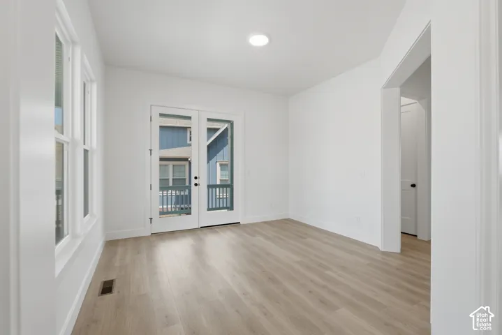 Recessed lighting, wood-finish flooring, white walls, multiple windows, and a double glass-panel door