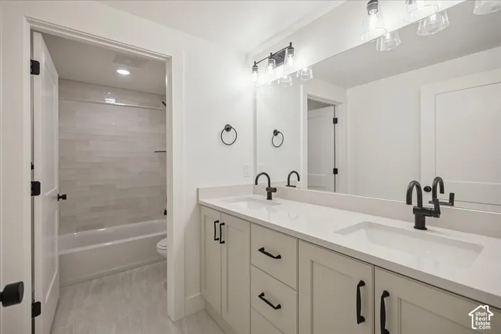 Double vanity featuring quartz countertops, undermount sinks, matte black fixtures, shaker-style cabinetry, and tiled shower surround