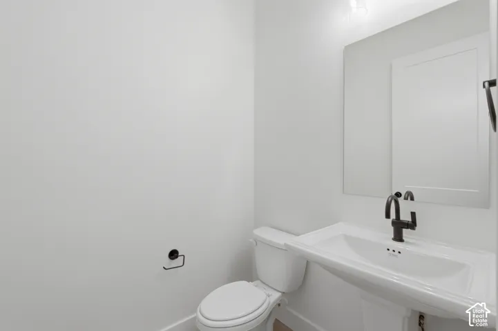 White pedestal sink with a matte black faucet, wall-mounted mirror, and white toilet
