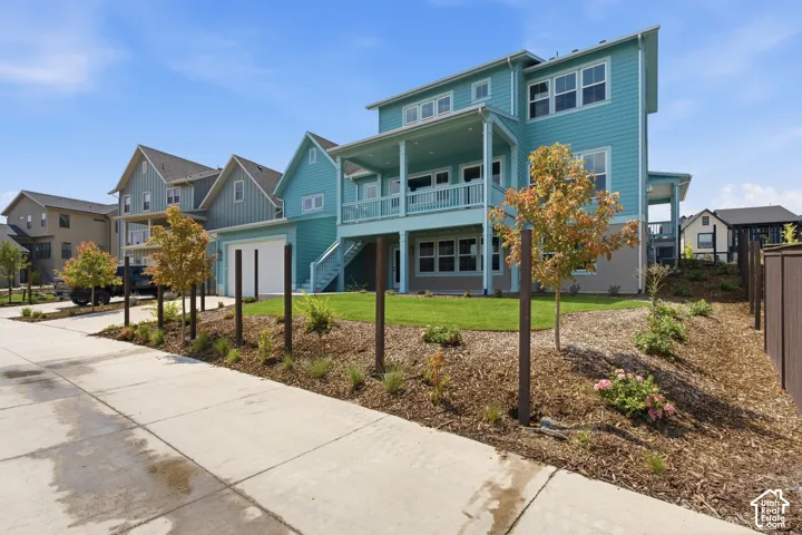 Two-story residence with a covered balcony, lower-level patio, attached garage, and landscaped grounds