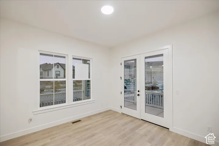 Neutral-toned walls, wood-finish flooring, dual-pane windows, and full-glass French doors opening to a porch