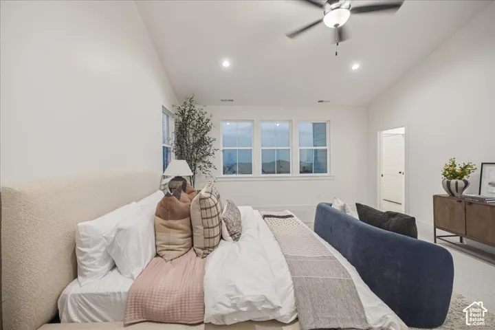 Primary Suite! Vaulted ceilings, neutral walls, carpeted flooring, triple-pane window configuration, and a central ceiling fan with integrated lighting
