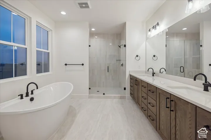 Freestanding soaking tub with matte black faucet, dual-sink vanity with stone countertop, frameless glass-enclosed shower, wood-finish cabinetry, and matte black hardware