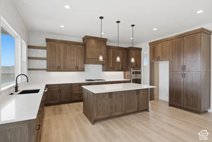 Chef's kitchen featuring rich wood cabinetry, a large center island with waterfall countertop, pendant lighting, stainless steel appliances, quartz counters, and wide-plank wood-finish flooring throughout the open layout
