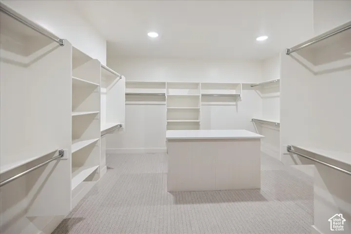 Walk-in closet featuring extensive built-in white shelving, integrated hanging rods, a central island with a smooth surface countertop, and neutral carpeting