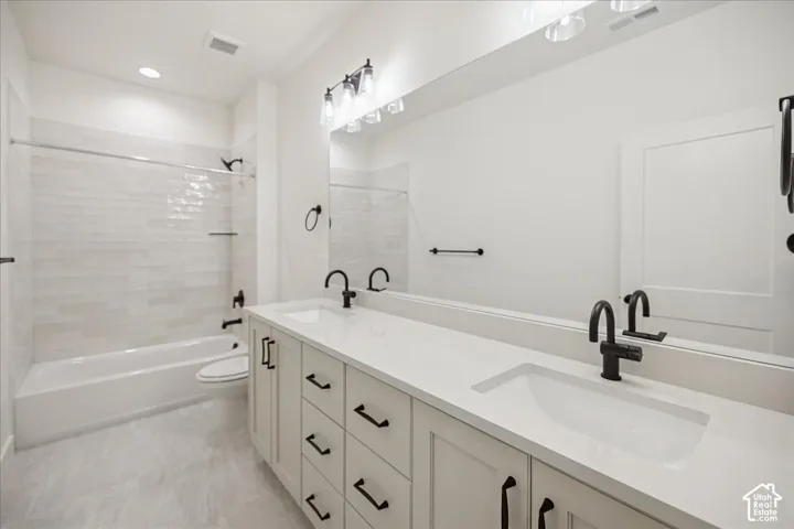 Dual-sink vanity with white stone-finish countertop, matte black hardware, subway-tiled tub surround, and oversized wall-to-wall mirror