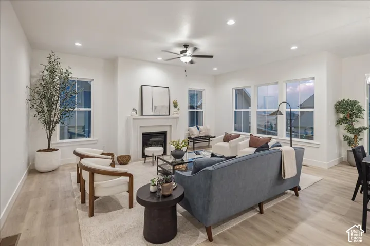 Living area featuring wood-finish flooring, a fireplace with a mantel, recessed lighting, a ceiling fan, and large windows