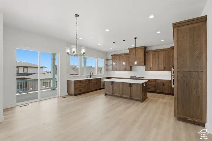 Spacious open-concept kitchen featuring warm wood cabinetry, white quartz countertops, a large center island with seating, stainless steel appliances, pendant lighting, recessed ceiling lights, and light wood-finish flooring throughout
