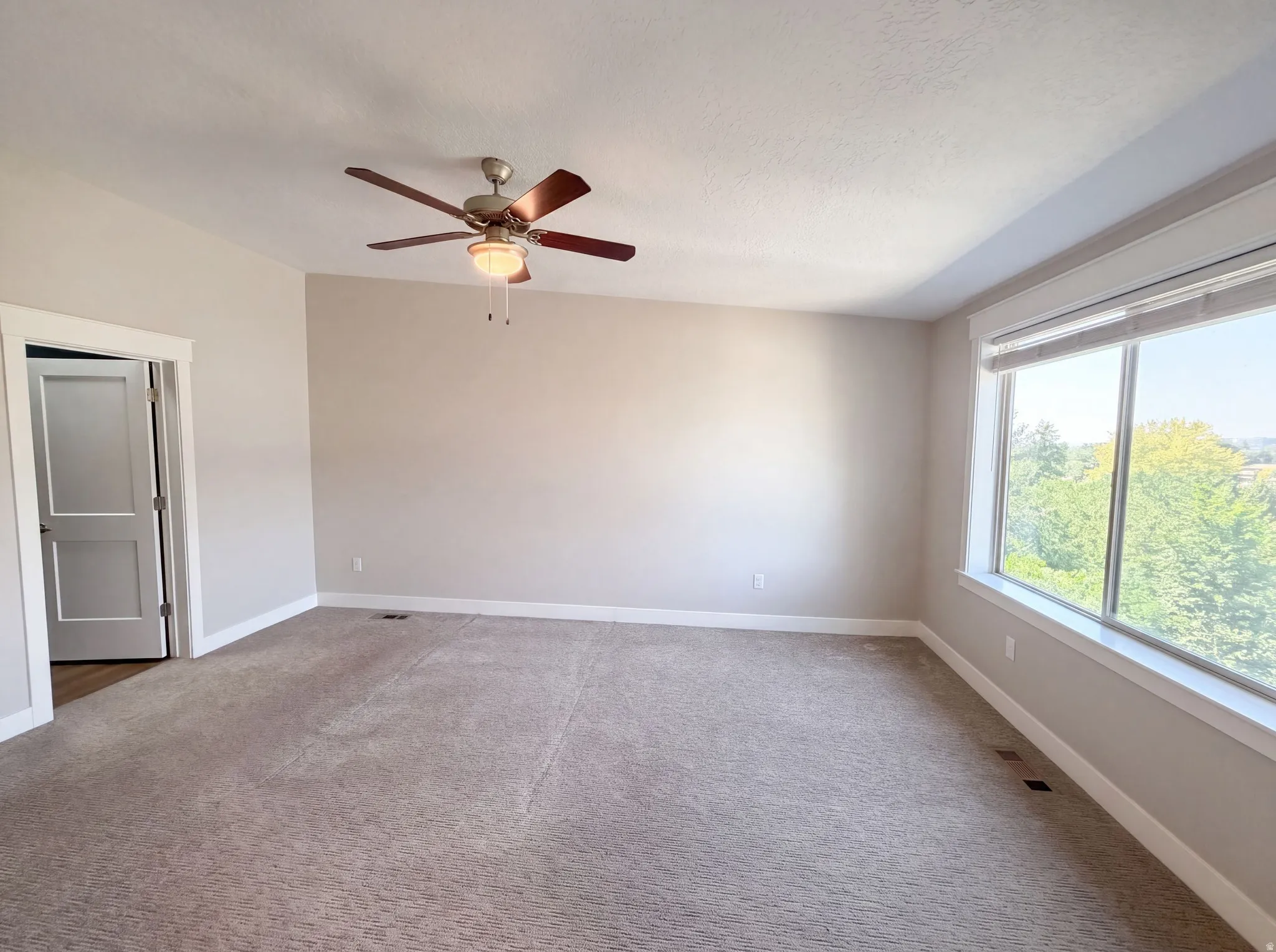 Expansive room featuring a large window, neutral carpeting, and a ceiling fan with integrated lighting