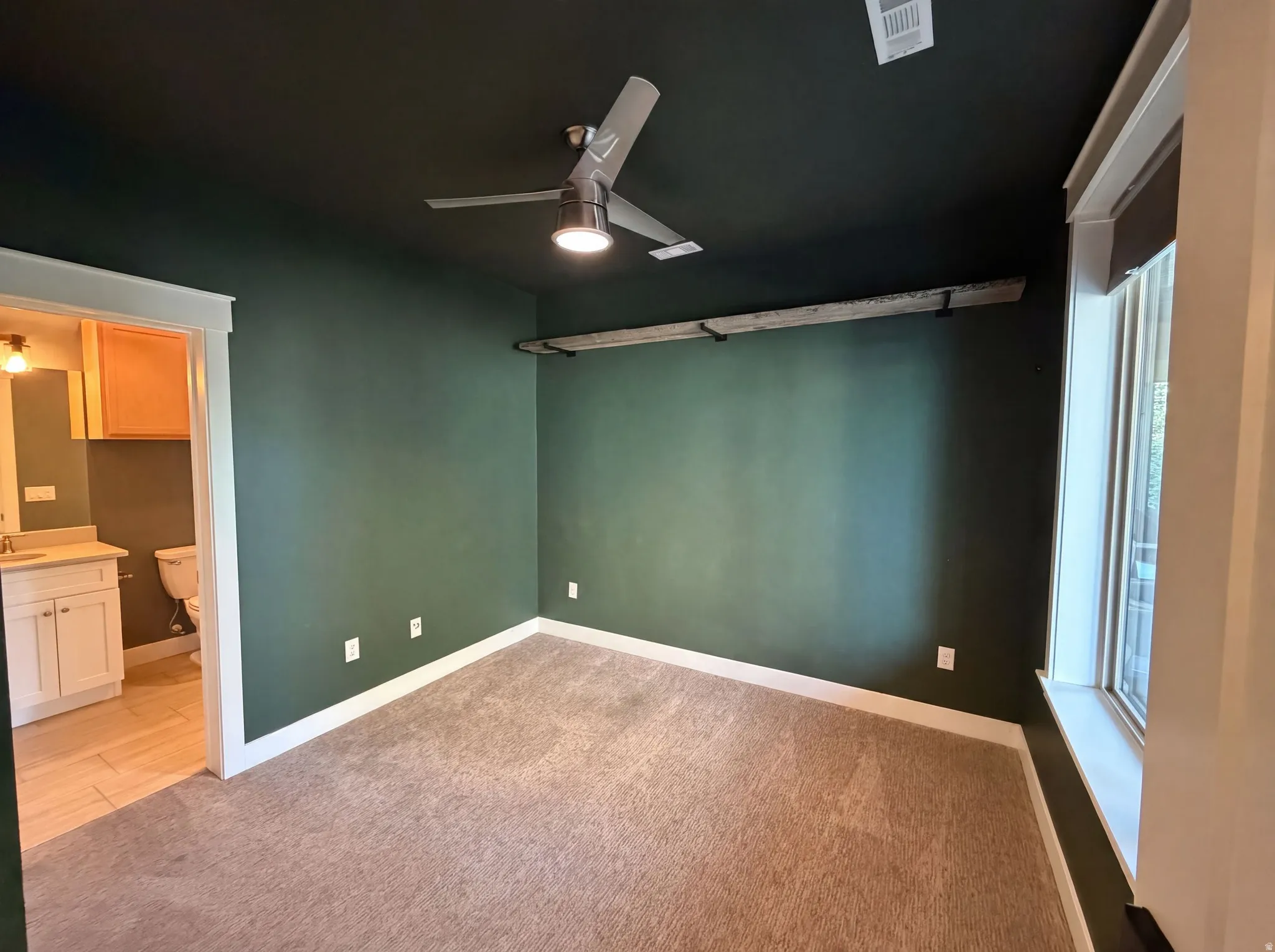 Textured carpeting, dark green accent walls, a contemporary ceiling fan, and a built-in window sill