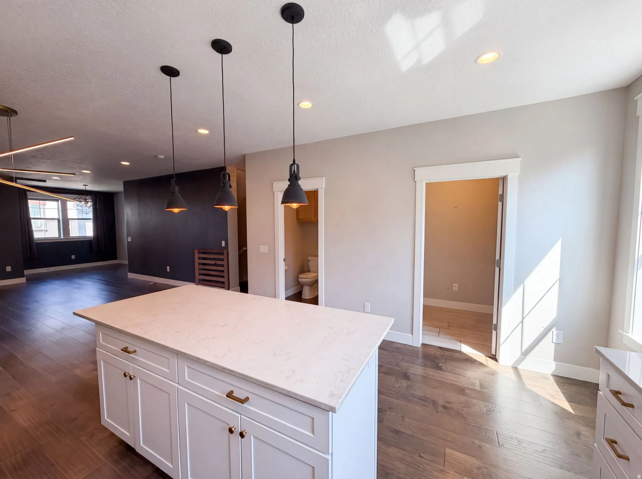 Kitchen island with white cabinetry and brass hardware, quartz countertop, wood-finish flooring, recessed lighting, and pendant lighting