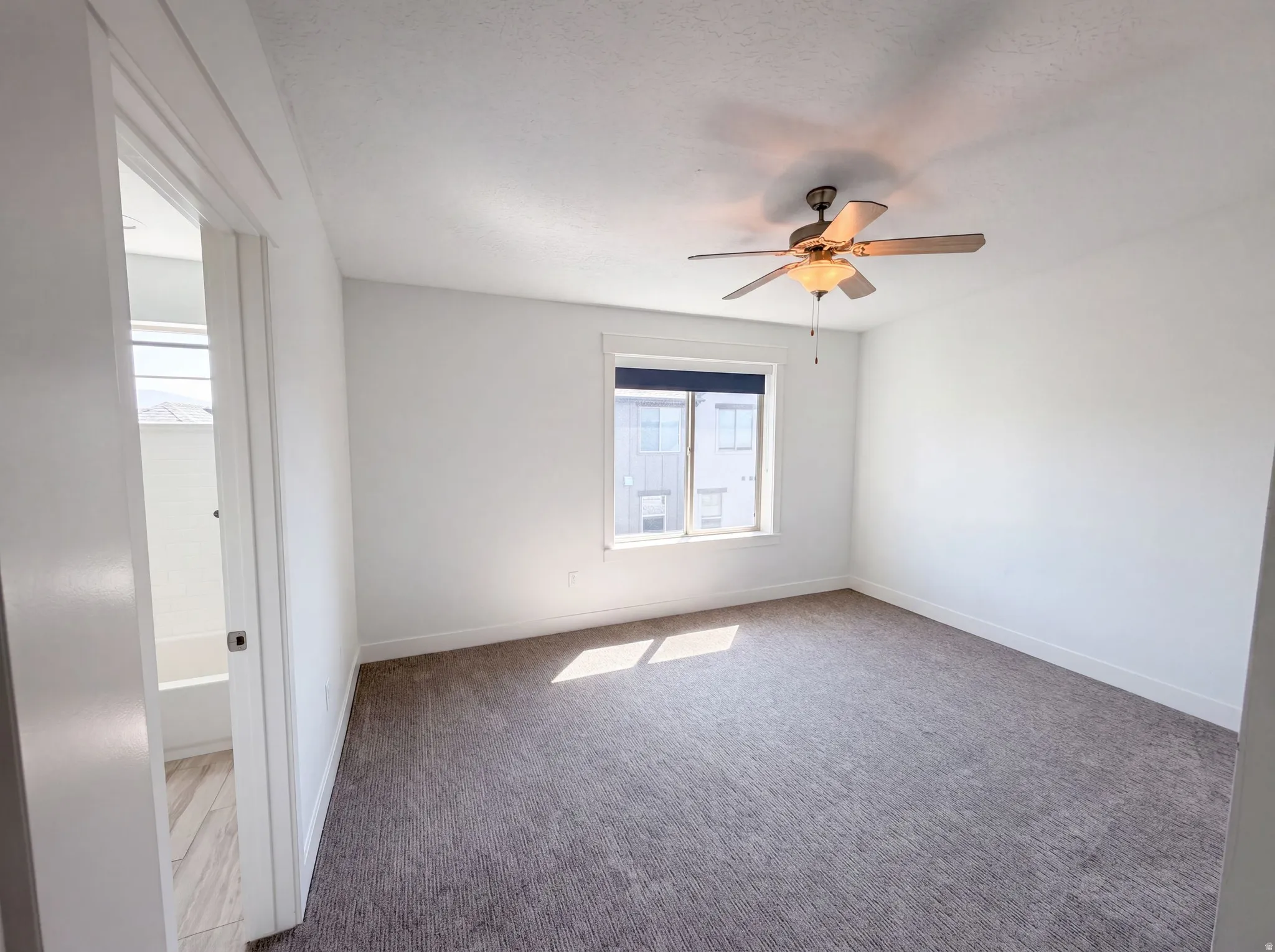 Spacious room featuring neutral carpeting, a ceiling fan with integrated lighting, and a single window with blinds