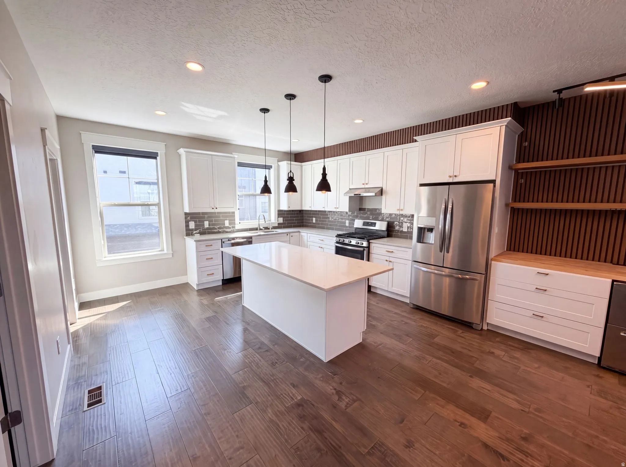Spacious kitchen with wood-finish flooring, white cabinetry, stainless steel appliances, and a central island with a solid surface countertop