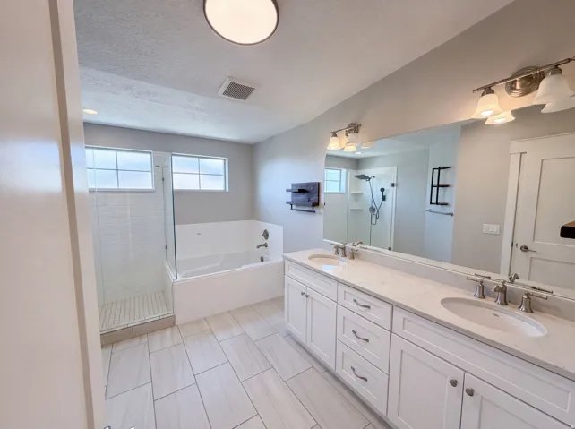 Dual vanity with undermount sinks and quartz countertops, walk-in shower with glass enclosure, separate soaking tub, and tile flooring