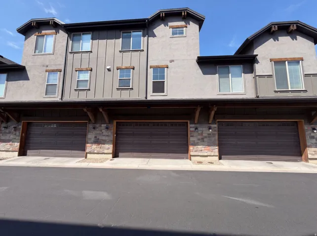 Multi-story exterior with stucco and board and batten siding, three individual garages, and stone facade accents