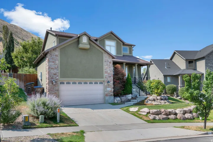 Two-story residence featuring a stone and stucco exterior, an attached garage, a paved driveway, and a landscaped front yard with rock retaining walls